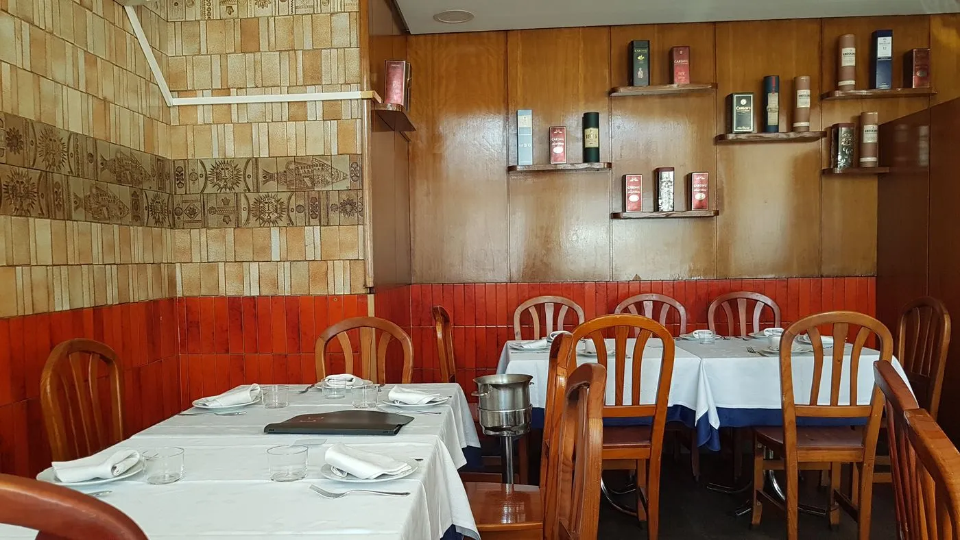Comedor con mesas de mantel blanco, sillas de madera y zócalo naranja