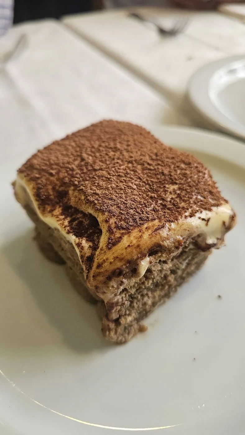 Porción de tiramisú con cacao por encima, en un plato blanco